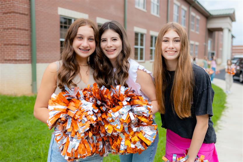 Three girls smile while holding pompoms